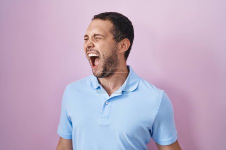 Photo for Hispanic man standing over pink background angry and mad screaming frustrated and furious, shouting with anger. rage and aggressive concept. - Royalty Free Image
