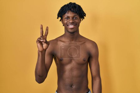 Photo for Young african man with dreadlocks standing shirtless showing and pointing up with fingers number two while smiling confident and happy. - Royalty Free Image