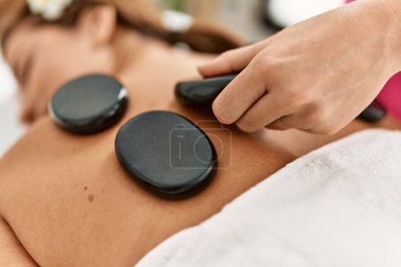 Photo for Young latin woman having back massage session using hot stones - Royalty Free Image