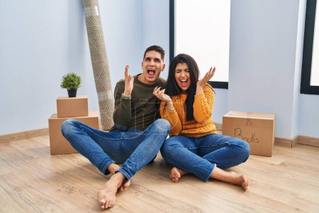 Téléchargez les photos : Young couple sitting on the floor at new home crazy and mad shouting and yelling with aggressive expression and arms raised. frustration concept. - en image libre de droit