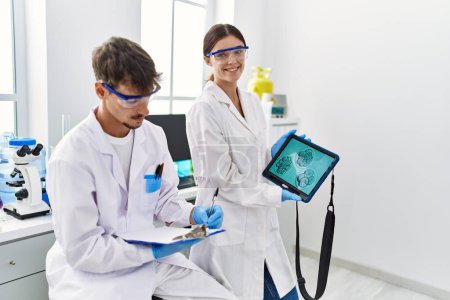 Foto de Compañeros hombres y mujeres vistiendo uniforme científico usando touchpad con imagen embrionaria en laboratorio - Imagen libre de derechos