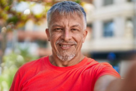 Photo for Middle age grey-haired man smiling confident making selfie by camera at park - Royalty Free Image