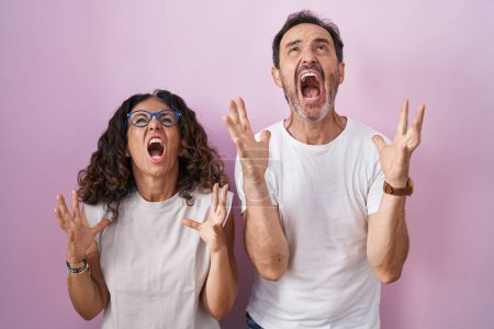 Photo for Middle age hispanic couple together over pink background crazy and mad shouting and yelling with aggressive expression and arms raised. frustration concept. - Royalty Free Image