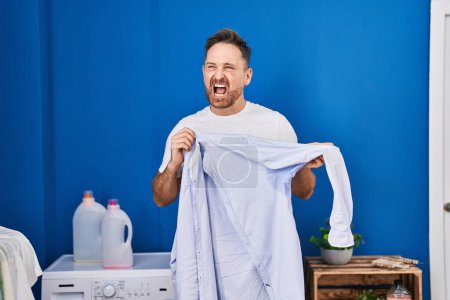 Photo for Middle age caucasian man holding shirt with sweat angry and mad screaming frustrated and furious, shouting with anger. rage and aggressive concept. - Royalty Free Image