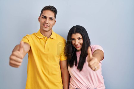 Téléchargez les photos : Jeune couple debout sur fond isolé approuvant faire un geste positif avec la main, pouces levés souriant et heureux pour le succès. geste gagnant. - en image libre de droit