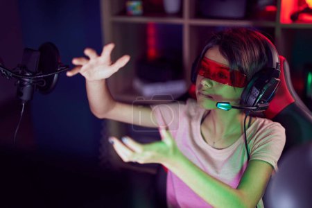 Téléchargez les photos : Adorable hispanic girl streamer playing video game using virtual reality glasses at gaming room - en image libre de droit