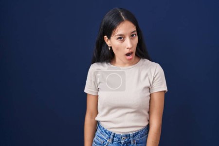 Foto de Mujer hispana joven de pie sobre fondo azul en la cara de choque, mirando escéptico y sarcástico, sorprendido con la boca abierta - Imagen libre de derechos