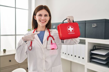 Photo for Young doctor woman holding first aid kit smiling happy pointing with hand and finger - Royalty Free Image
