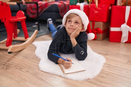 Téléchargez les photos : Adorable tout-petit écrit sur un cahier couché près d'un arbre de Noël à la maison - en image libre de droit