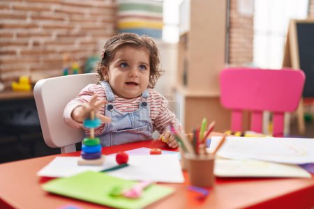Foto de Adorable chica hispana jugando con aros juego sentado en la mesa en el jardín de infantes - Imagen libre de derechos