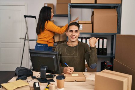 Photo for Young woman and man working at small business ecommerce pointing thumb up to the side smiling happy with open mouth - Royalty Free Image