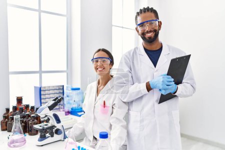 Téléchargez les photos : Man and woman scientist partners holding clipboard looking to the camera at laboratory - en image libre de droit