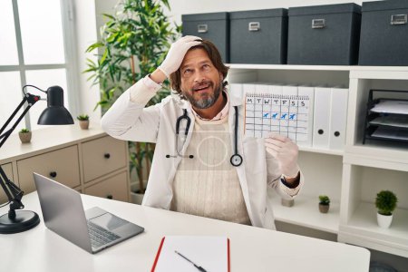 Photo for Handsome middle age doctor man holding holidays calendar stressed and frustrated with hand on head, surprised and angry face - Royalty Free Image