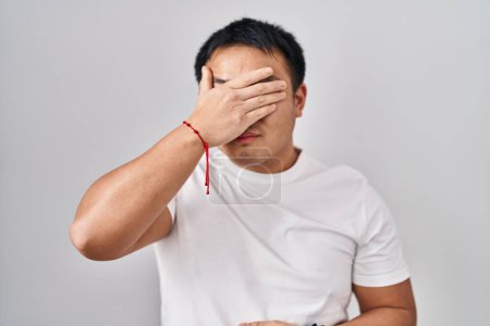 Téléchargez les photos : Young chinese man standing over white background covering eyes with hand, looking serious and sad. sightless, hiding and rejection concept - en image libre de droit