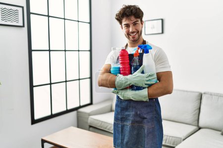 Foto de Young hispanic man doing chores holding cleaning products at home - Imagen libre de derechos