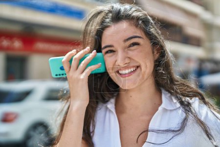 Foto de Mujer hispana joven sonriendo confiado escuchando mensaje de audio por el teléfono inteligente en la calle - Imagen libre de derechos