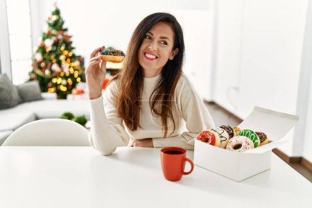 Foto de Mujer hispana de mediana edad desayunando sentada en la mesa junto al árbol de Navidad en casa - Imagen libre de derechos