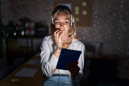 Photo for Young blonde woman working at the office at night looking stressed and nervous with hands on mouth biting nails. anxiety problem. - Royalty Free Image