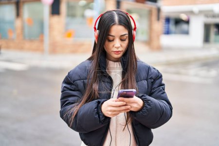 Téléchargez les photos : Jeune belle femme hispanique écoutant de la musique avec une expression détendue dans la rue - en image libre de droit