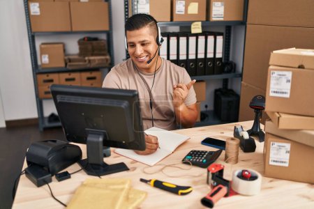 Téléchargez les photos : Jeune homme hispanique travaillant dans une petite entreprise commerce électronique souriant heureux pointant avec la main et le doigt sur le côté - en image libre de droit