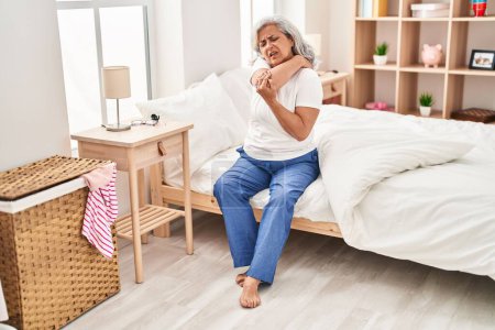Téléchargez les photos : Middle age woman suffering for back pain sitting on bed at bedroom - en image libre de droit