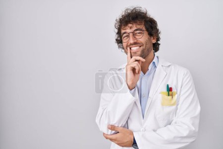 Foto de Hispanic young man wearing doctor uniform looking confident at the camera smiling with crossed arms and hand raised on chin. thinking positive. - Imagen libre de derechos