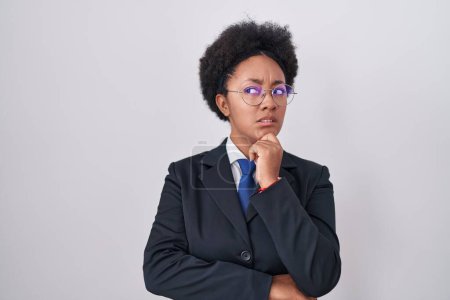 Foto de Beautiful african woman with curly hair wearing business jacket and glasses thinking worried about a question, concerned and nervous with hand on chin - Imagen libre de derechos