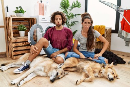 Photo for Young hispanic couple doing laundry with dogs depressed and worry for distress, crying angry and afraid. sad expression. - Royalty Free Image