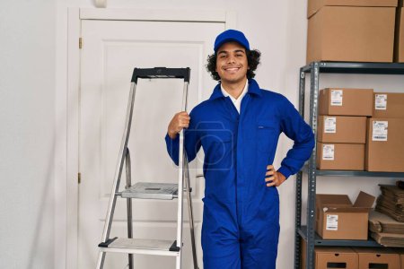 Foto de Joven técnico hispano sosteniendo escalera de pie en la oficina - Imagen libre de derechos