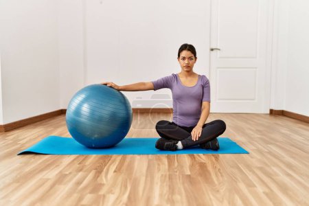 Photo for Young latin woman stretching using fit ball at sport center - Royalty Free Image
