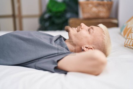 Téléchargez les photos : Jeune homme caucasien souriant confiant couché sur le lit dans la chambre - en image libre de droit