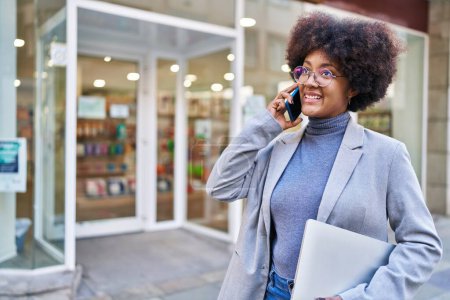 Téléchargez les photos : Afro-américaine femme exécutif parler sur smartphone tenant ordinateur portable à la rue - en image libre de droit