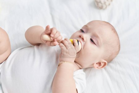 Photo for Adorable caucasian baby lying on bed sucking maraca toy at bedroom - Royalty Free Image
