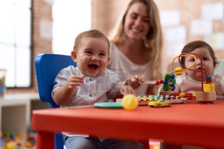 Foto de Profesor y estudiantes de preescolar jugando con juguetes sentados en la mesa en el jardín de infantes - Imagen libre de derechos