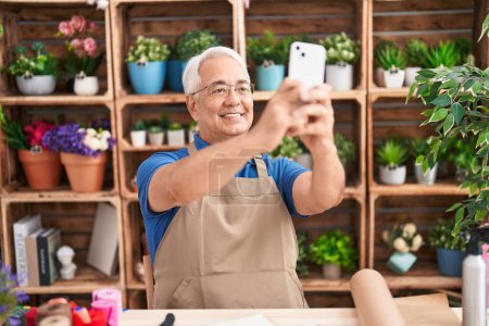 Téléchargez les photos : Moyen Age homme aux cheveux gris fleuriste faire selfie par smartphone chez le fleuriste - en image libre de droit