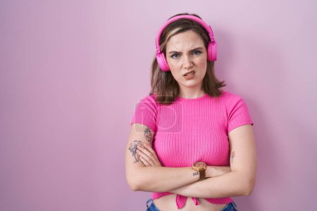 Foto de Blonde caucasian woman listening to music using headphones skeptic and nervous, disapproving expression on face with crossed arms. negative person. - Imagen libre de derechos