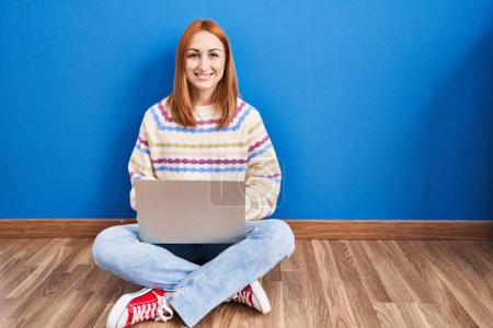 Téléchargez les photos : Jeune femme utilisant un ordinateur portable à la maison assis sur le sol avec un sourire heureux et cool sur le visage. chanceux. - en image libre de droit