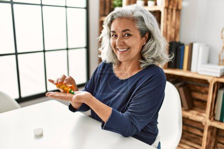 Téléchargez les photos : Middle age grey-haired woman taking pills sitting on the table at home. - en image libre de droit