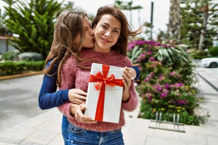 Téléchargez les photos : Mère et fille s'embrassant et s'embrassant tenant cadeau d'anniversaire au parc - en image libre de droit