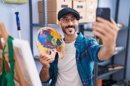 Téléchargez les photos : Jeune homme hispanique artiste tenant palette faire selfie par smartphone au studio d'art - en image libre de droit