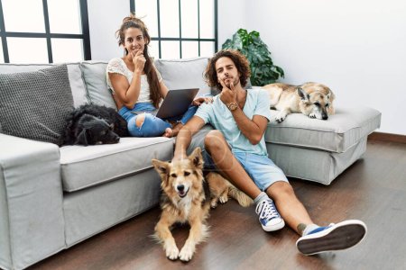 Photo for Young hispanic couple with dogs relaxing at home looking confident at the camera smiling with crossed arms and hand raised on chin. thinking positive. - Royalty Free Image