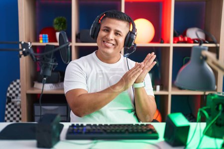 Téléchargez les photos : Jeune homme hispanique jouant à des jeux vidéo applaudissant et applaudissant heureux et joyeux, souriant mains fières ensemble - en image libre de droit