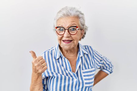 Foto de Mujer mayor con el pelo gris de pie sobre fondo blanco haciendo un gesto feliz pulgares hacia arriba con la mano. aprobando la expresión mirando a la cámara mostrando éxito. - Imagen libre de derechos