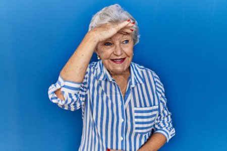 Photo for Senior woman with grey hair standing over blue background very happy and smiling looking far away with hand over head. searching concept. - Royalty Free Image
