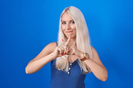 Foto de Caucasian woman standing over blue background rejection expression crossing fingers doing negative sign - Imagen libre de derechos