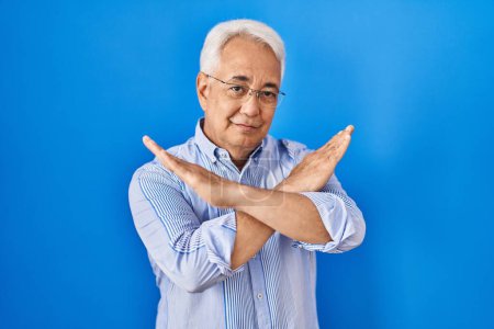 Photo for Hispanic senior man wearing glasses rejection expression crossing arms doing negative sign, angry face - Royalty Free Image