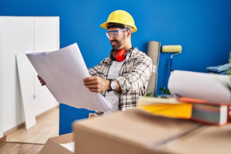 Photo for Young hispanic man worker smiling confident looking blueprints at new home - Royalty Free Image