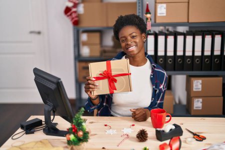 Téléchargez les photos : Femme afro-américaine debout par mannequin à la petite entreprise sur Noël regardant positif et heureux debout et souriant avec un sourire confiant montrant les dents - en image libre de droit