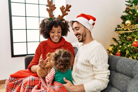 Téléchargez les photos : Couple and daughter playing with teddy bear sitting by christmas tree at home - en image libre de droit
