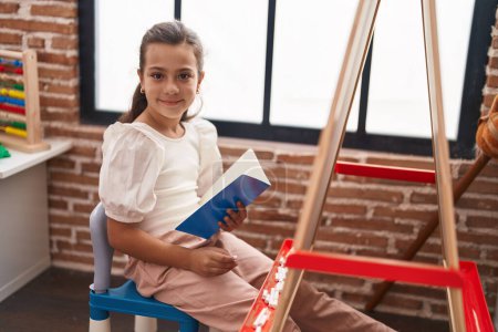 Téléchargez les photos : Adorable hispanique fille étudiant livre de lecture assis sur la chaise à la salle de classe - en image libre de droit